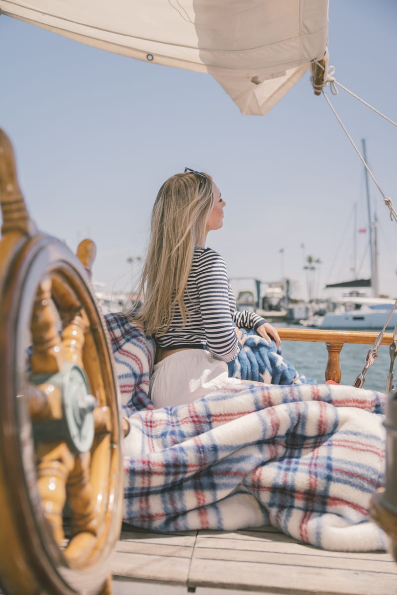 Woman sitting on a boat deck with a plaid blanket, looking out at the water.