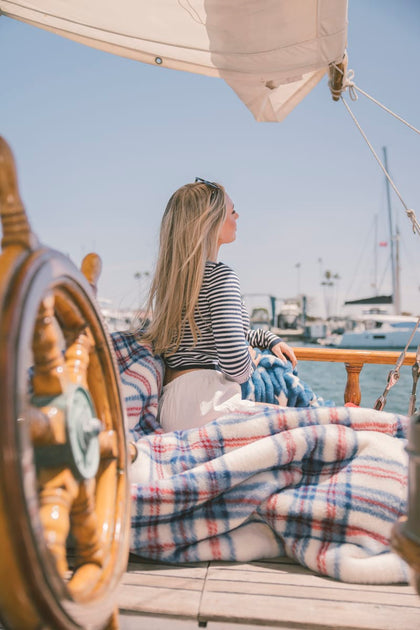 Woman sitting on a boat deck with a plaid blanket, looking out at the water.