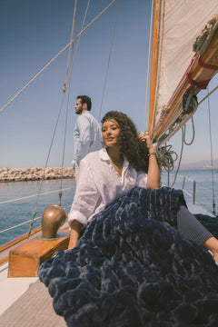 Woman holding a navy blanket on a sailboat with a man in the background.