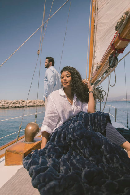 Woman holding a navy blanket on a sailboat with a man in the background.
