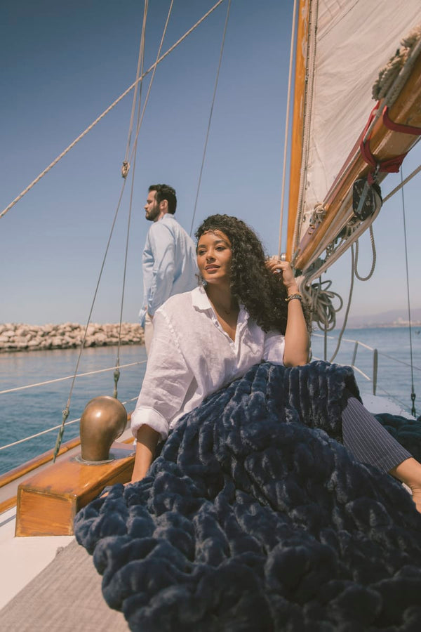 Woman holding a navy blanket on a sailboat with a man in the background.