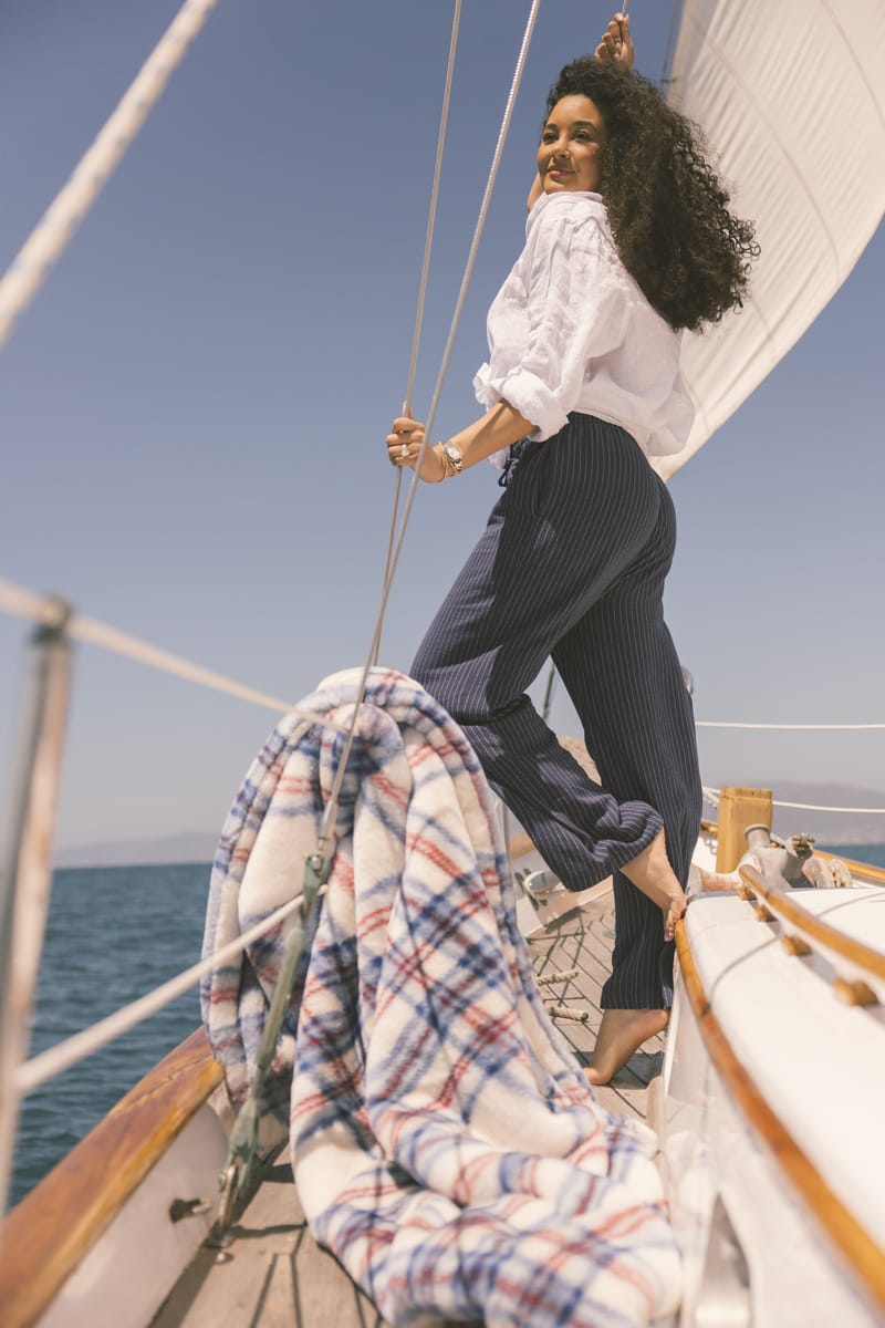 Woman on a sailboat with a clear blue sky and ocean background by a patriotic plaid blanket.
