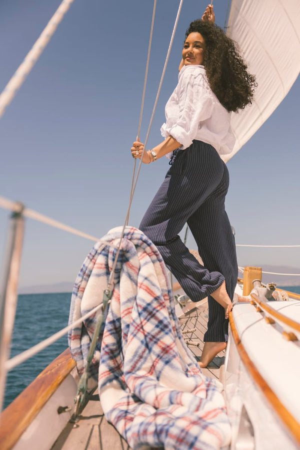 Woman on a sailboat with a clear blue sky and ocean background by a patriotic plaid blanket.