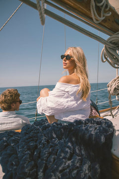 Woman in a white off-shoulder top on a sailboat with a clear blue sky and ocean with a navy Minky Couture blanket.