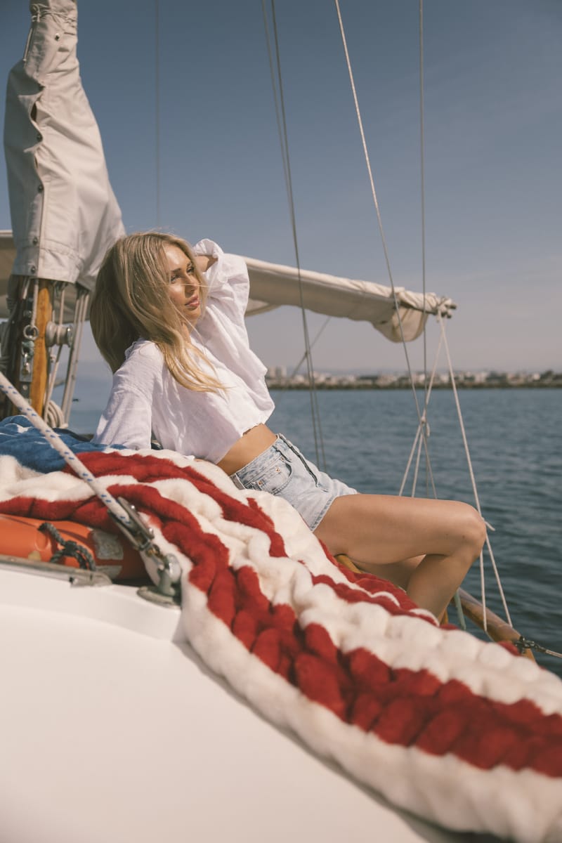 Woman sitting on an American flag blanket on a sailboat with a clear blue sky and water background