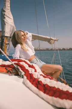 Woman sitting on an American flag blanket on a sailboat with a clear blue sky and water background