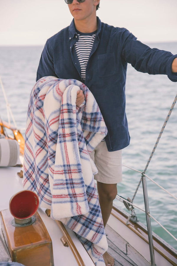 Person on a boat with a patriotic color themed plaid blanket and sunglasses