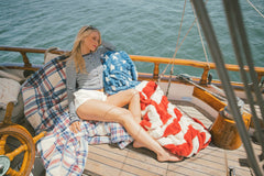 Woman sitting on a boat with a plaid blanket, surrounded by water.