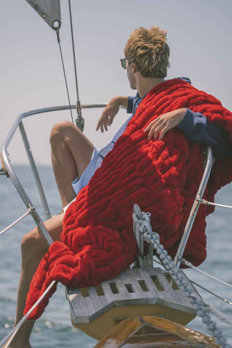 Person sitting on a sailboat with a red Minky Couture blanket wrapped around them, wearing sunglasses.