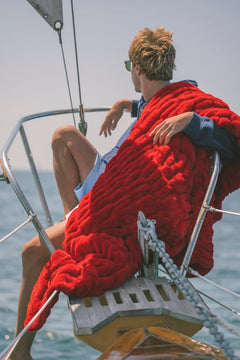 Person sitting on a sailboat with a red Minky Couture blanket wrapped around them, wearing sunglasses.