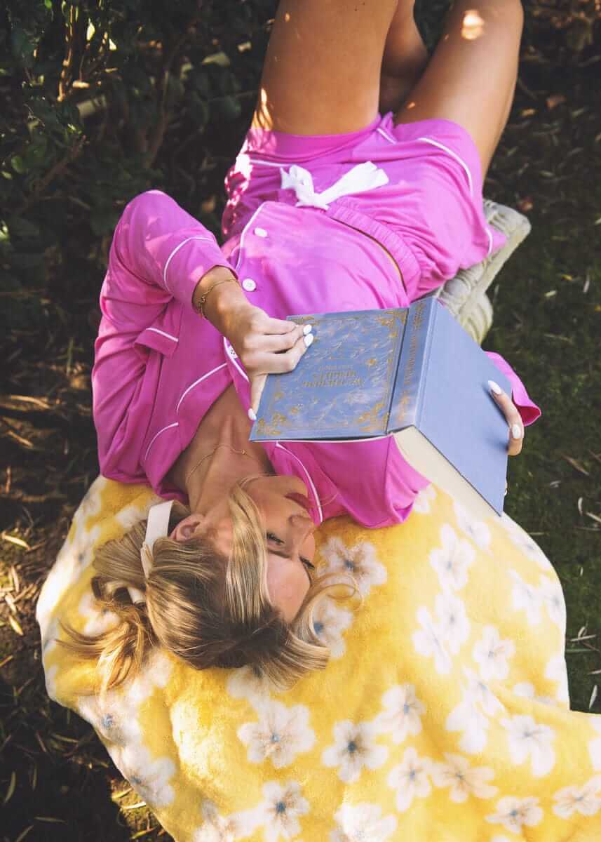 Woman relaxing outdoors on a Minky Couture Lush Butter Yellow Floral Blanket while reading a book.
