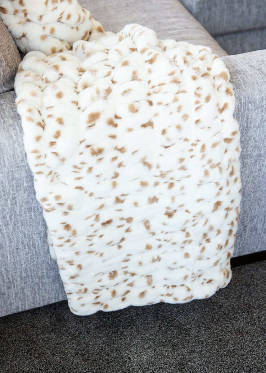 Hugs Spotted Fawn Blanket draped elegantly over a sofa, featuring a soft cream background with playful tan spots.