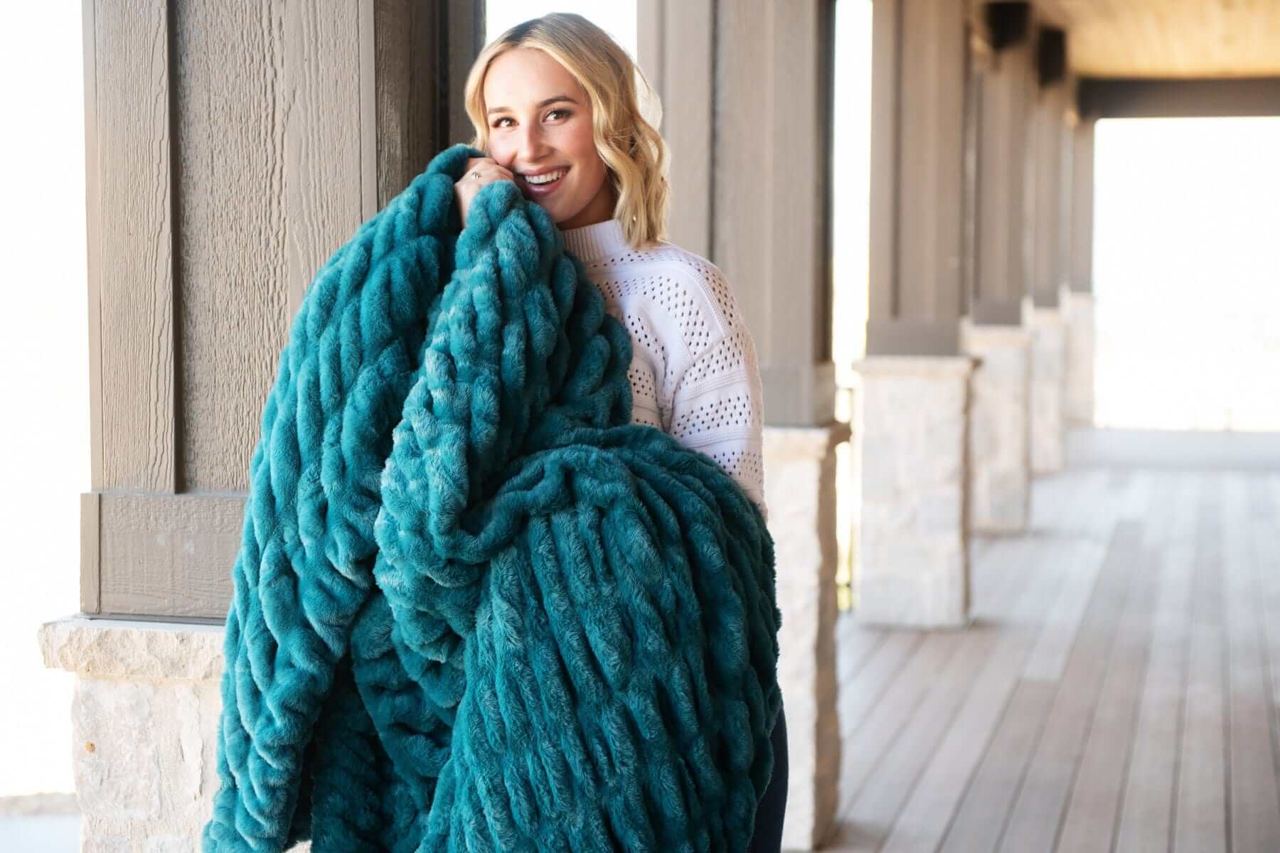 A woman holding the Hugs Deep Lake Blanket, showcasing its plush texture and deep blue color.