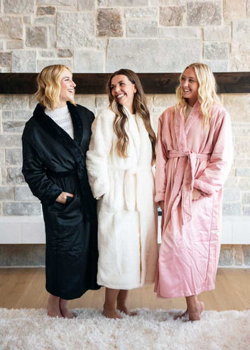 Three women wearing Minky Couture stylish robes, in black, pink and white colors, posing in a cozy setting.