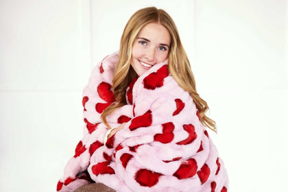 Woman snuggling with the Hugs Heart Red Blanket featuring red hearts on a soft pink background.