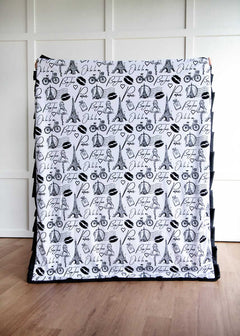 Patterned A Day In Paris blanket with black and white design on a wooden floor.