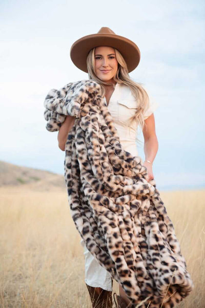 Woman standing in a field holding a leopard-print Minky Couture faux fur blanket.