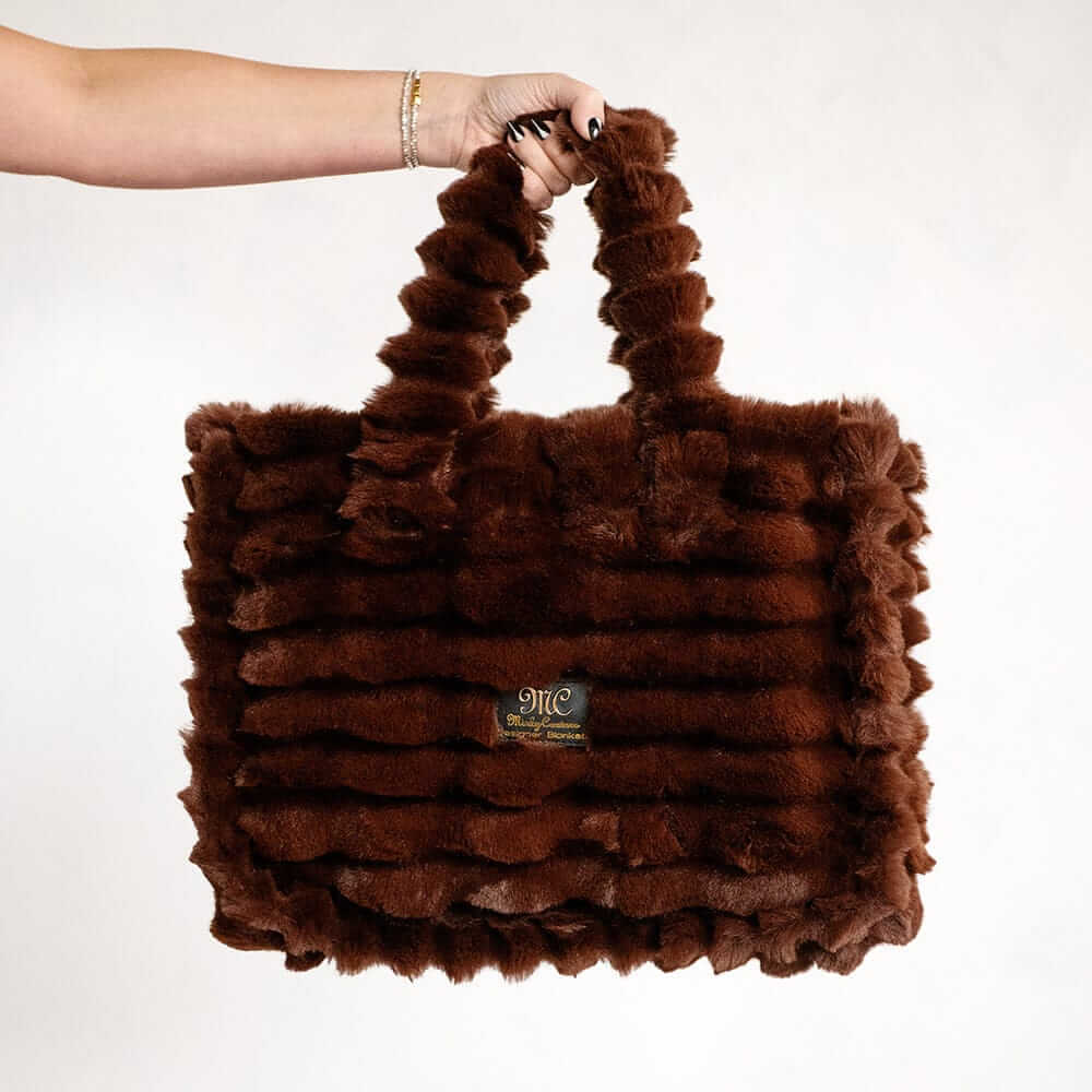 Hand holding a brown Minky Couture Annie bag with plush textured fabric against a white background.