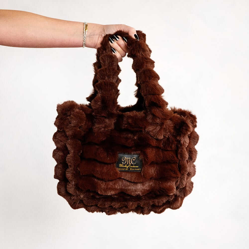 Hand holding a brown Minky Couture Annie bag with plush textured fabric against a white background.