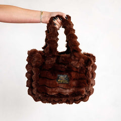 Hand holding a brown Minky Couture Annie bag with plush textured fabric against a white background.
