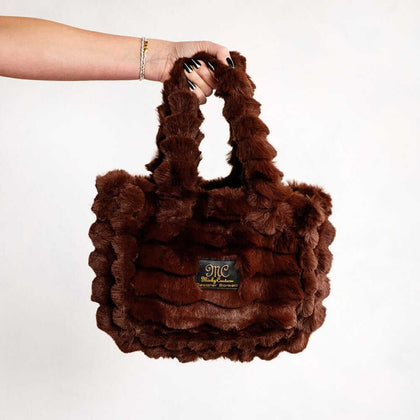 Hand holding a brown Minky Couture Annie bag with plush textured fabric against a white background.