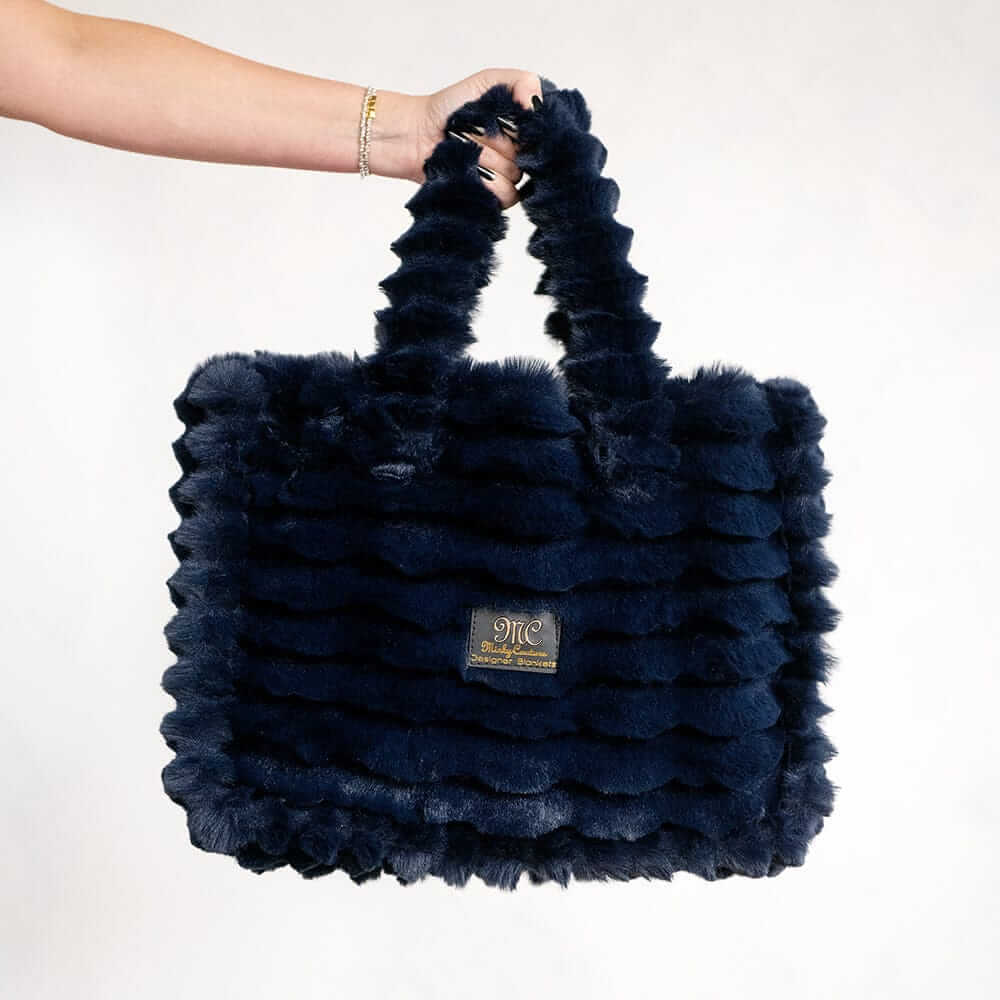 Hand holding a navy blue Minky Couture Annie bag with plush textured fabric against a white background.