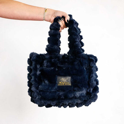 Hand holding a navy blue Minky Couture Annie bag with plush textured fabric against a white background.