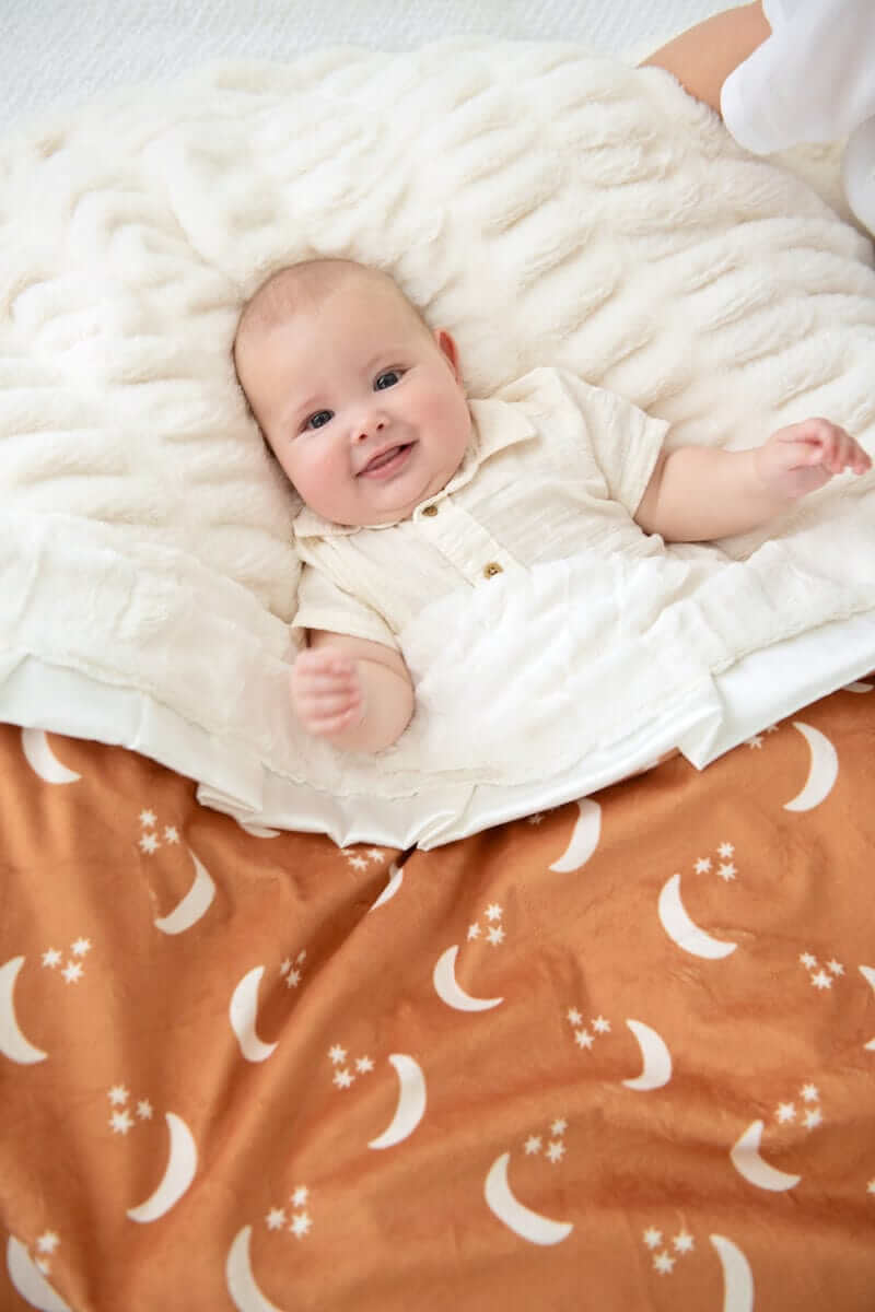 Infant lying on a plush blanket featuring Minky Couture Shining Moon Copper design with cream half-moons and stars.