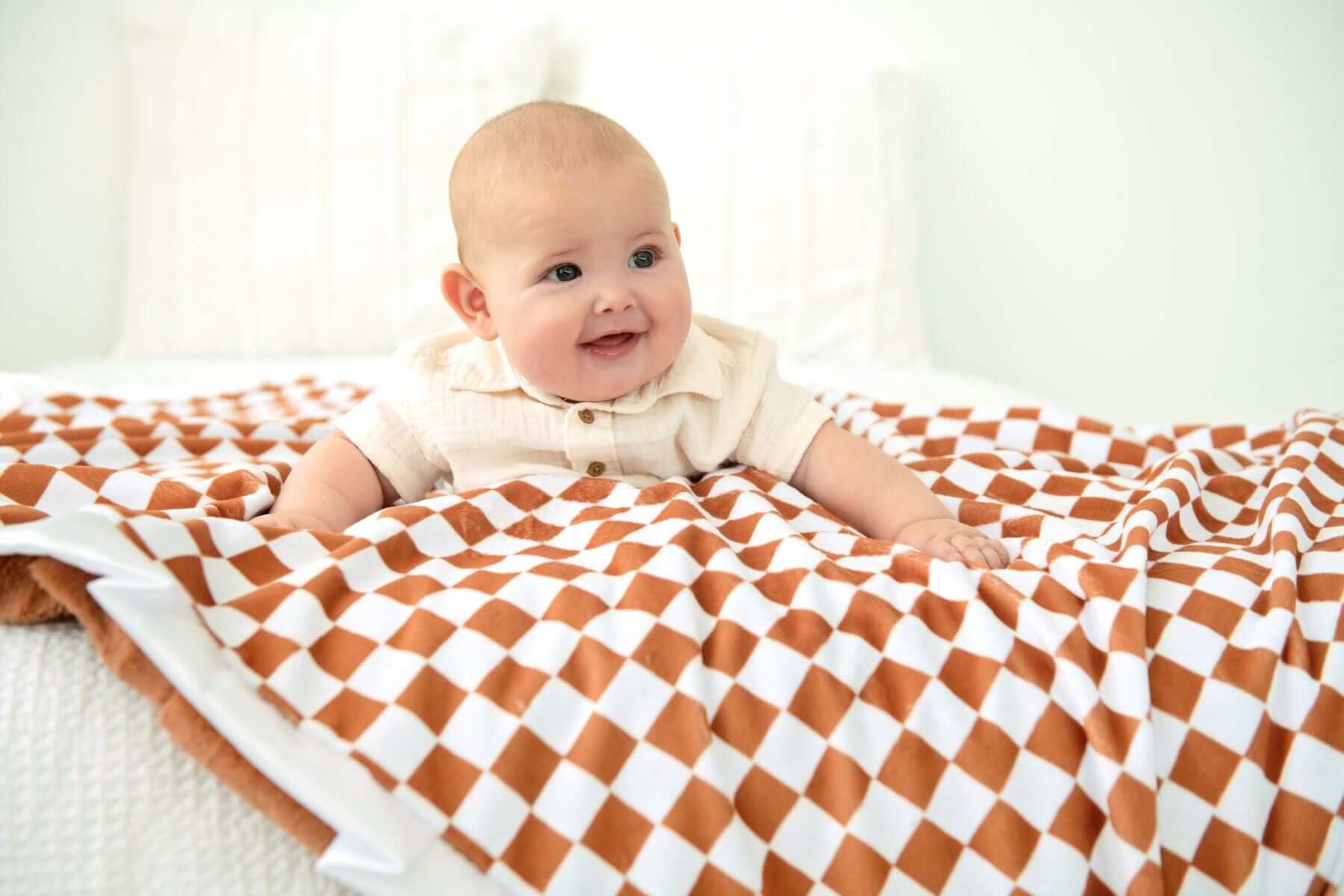 A baby smiling on a Checkered Copper Blanket featuring a hazelnut brown and cream checkered pattern.