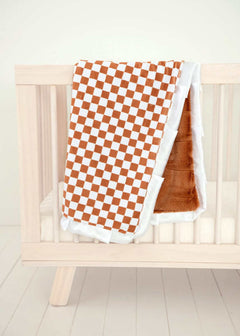 Checkered Copper Blanket draped over a wooden crib, featuring a hazelnut brown and cream checkered pattern with plush backing.