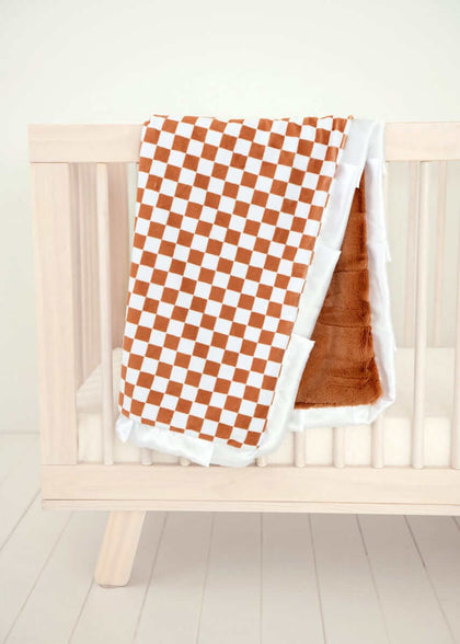 Checkered Copper Blanket draped over a wooden crib, featuring a hazelnut brown and cream checkered pattern with plush backing.
