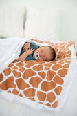 Cute baby sleeping on a Giraffe Blanket featuring a warm giraffe pattern in rusty brown and cream.