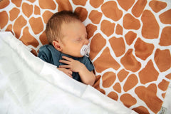 Minky Couture Giraffe Blanket featuring a classic giraffe pattern with a baby sleeping peacefully underneath.