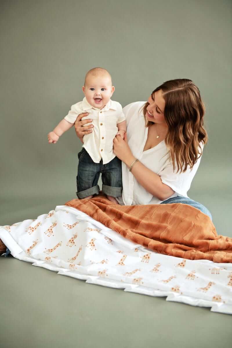 Mom and baby joyfully interact with the Little Giraffe Blanket featuring playful giraffes and soft minky.