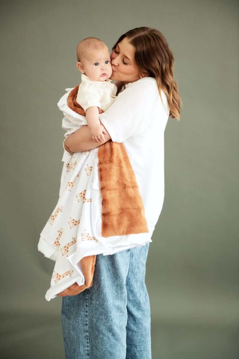 Mom cuddling baby with Minky Couture Little Giraffe Blanket featuring giraffe designs and plush backing.