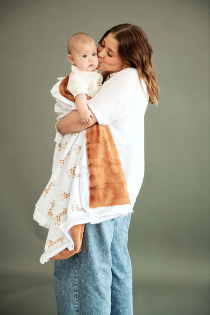 Mom cuddling baby with Minky Couture Little Giraffe Blanket featuring giraffe designs and plush backing.