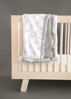 Cozy Shining Stars Blanket draped over a crib, featuring gold and silver star clusters on white, with a plush silver backing.