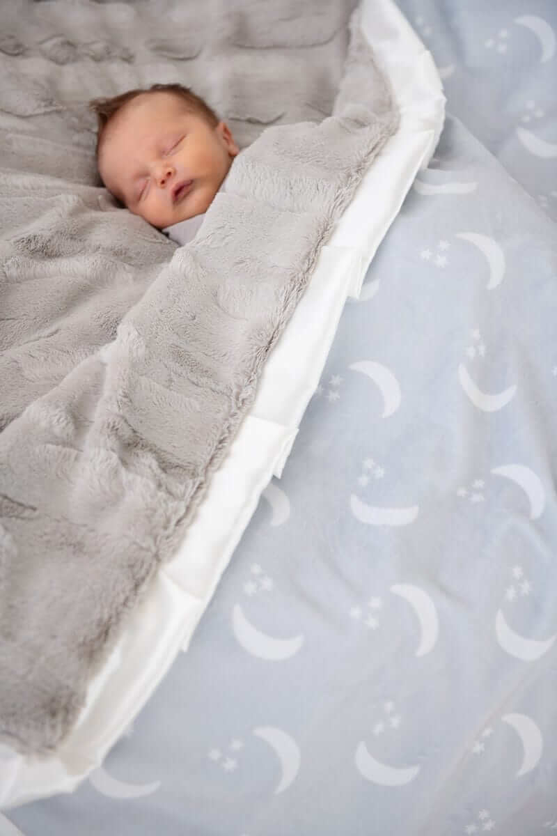 Baby sleeping peacefully under the Minky Couture Shining Moon Silver Blanket featuring soft gray and dreamy moon design.