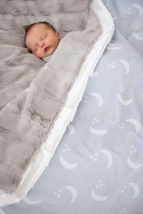 Baby sleeping peacefully under the Minky Couture Shining Moon Silver Blanket featuring soft gray and dreamy moon design.