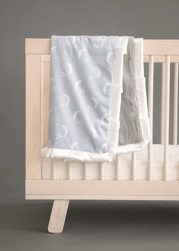 Minky CoutureShining Moon Silver Blanket draped over a crib, featuring a soft gray design with moons and stars.