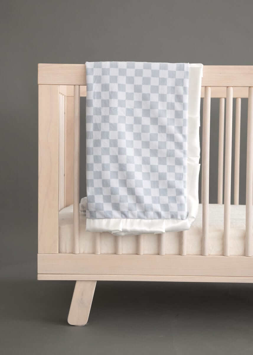 Minky Couture Checkered Silver Blanket draped over a wooden crib, featuring a classic light and dark gray checkered pattern.