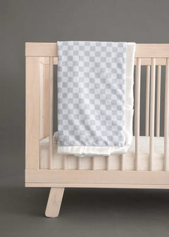 Minky Couture Checkered Silver Blanket draped over a wooden crib, featuring a classic light and dark gray checkered pattern.