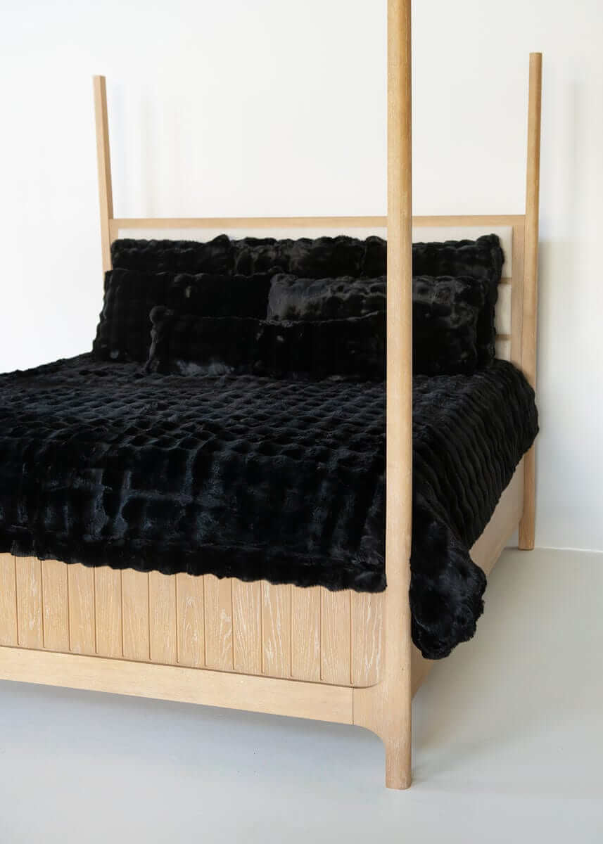 Black Minky Couture duvet and pillows styled on a wooden canopy bed against a white background.