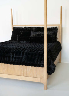 Black Minky Couture duvet and pillows styled on a wooden canopy bed against a white background.