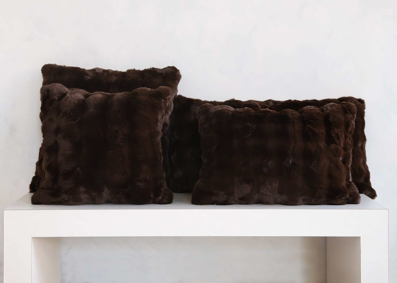 Dark brown Chocolate Cloud Sham faux fur throw pillows arranged on a white shelf.