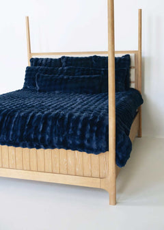 Navy blue Minky Couture duvet and pillows styled on a wooden canopy bed against a white background.