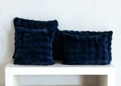 Navy blue Cloud Sham faux fur throw pillows arranged on a white shelf.