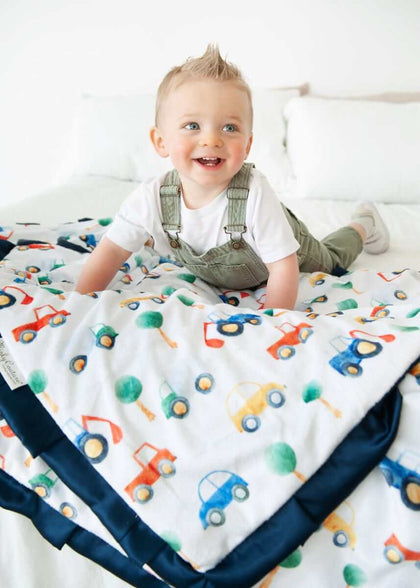 Happy toddler playing on a Cars Blanket featuring colorful cars and tractors.