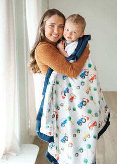 Mom and child snuggled in a colorful Cars Blanket featuring cars and tractors with a navy plush backing.