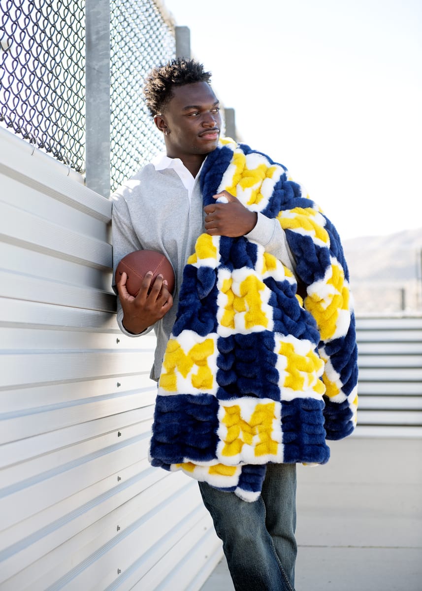 University of Michigan Wolverines Blanket draped over a young man holding a football, showcasing its cozy design.